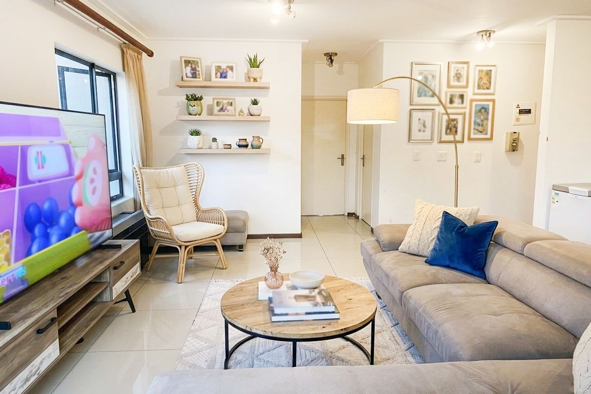 A bright and well-maintained living room featuring neutral tiled flooring, floating wall shelves, and modern recessed lighting, creating a comfortable and inviting atmosphere.