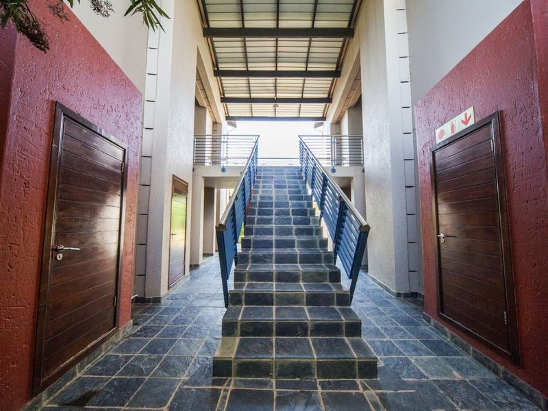 A well-maintained apartment complex hallway featuring a central tiled staircase with metal handrails and covered overhead structure.