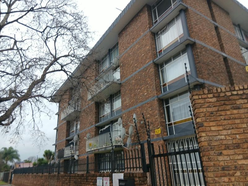 A multi-story apartment building featuring a face brick facade, individual balconies, and secure perimeter fencing with electric security measures.