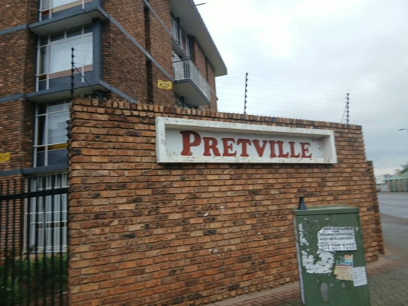 Exterior view of the Pretville apartment complex featuring a brick boundary wall, electric fencing, and multi-story residential building facade.