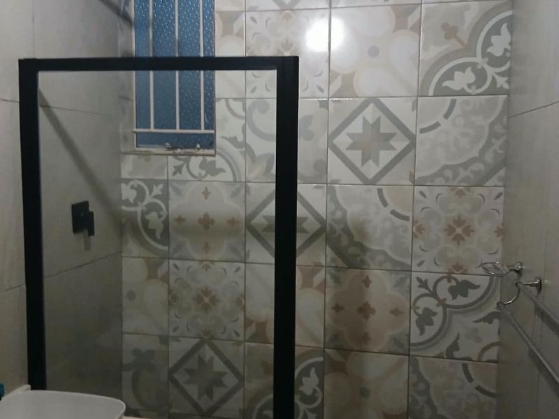 A modern bathroom featuring a glass shower enclosure, patterned decorative wall tiles, a vessel sink on a vanity countertop, and a small window with security bars.