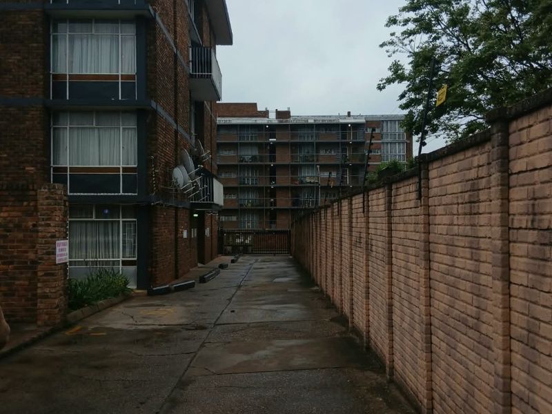 Rear exterior view of the apartment complex featuring a concrete driveway, brick boundary wall, and multi-story residential building facade.