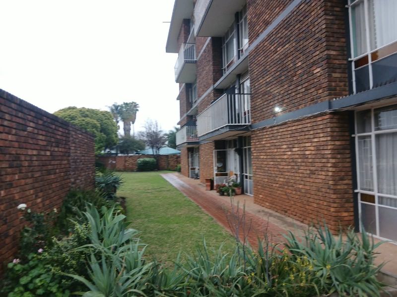 Rear view of a multi-story apartment building featuring face brick construction, private balconies, and a shared garden area with a paved walkway.