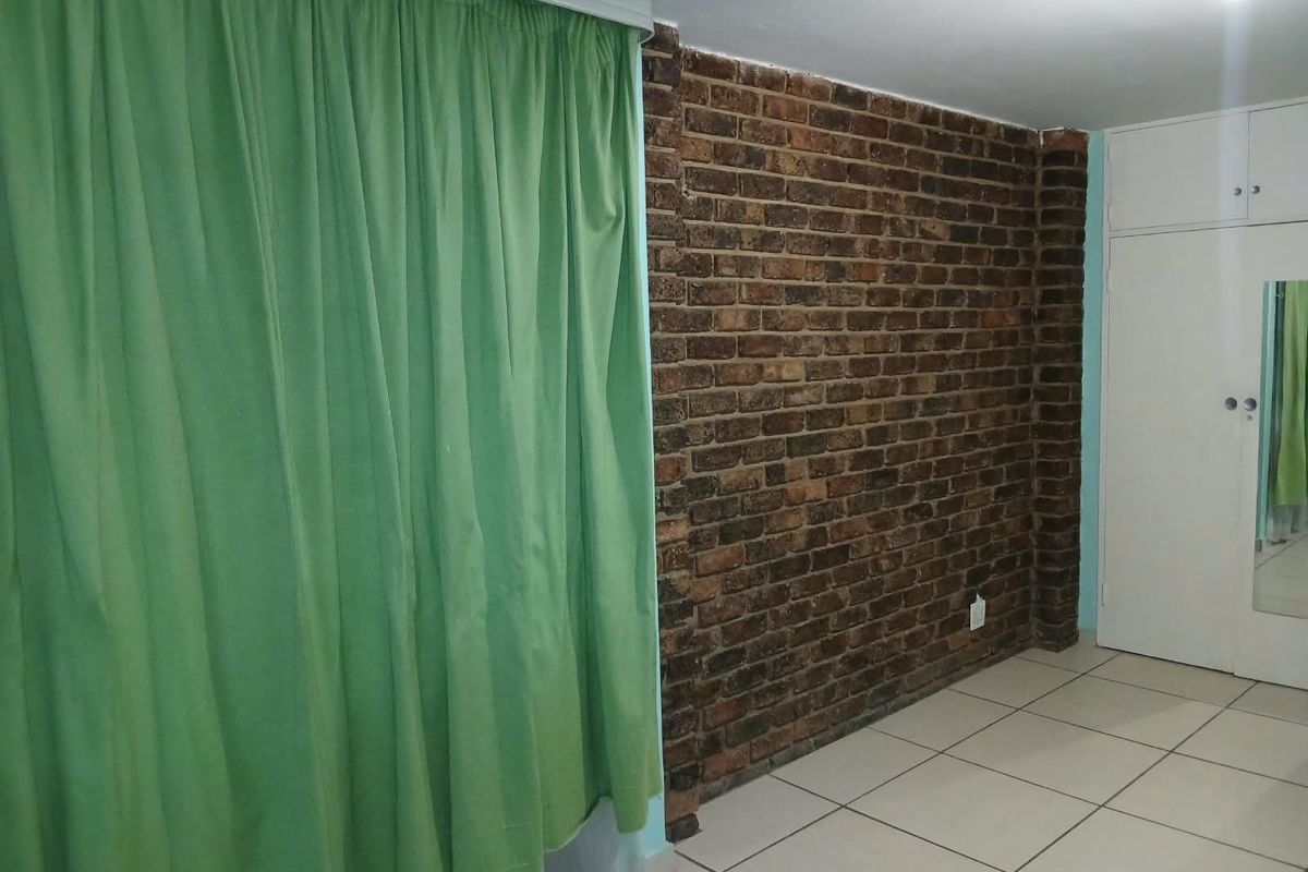 Bedroom featuring an exposed brick accent wall, tiled flooring, and built-in storage cupboards.