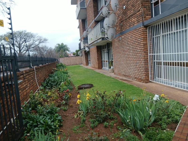 Exterior view of the apartment building featuring a brick facade, ground floor garden area, and security fencing.