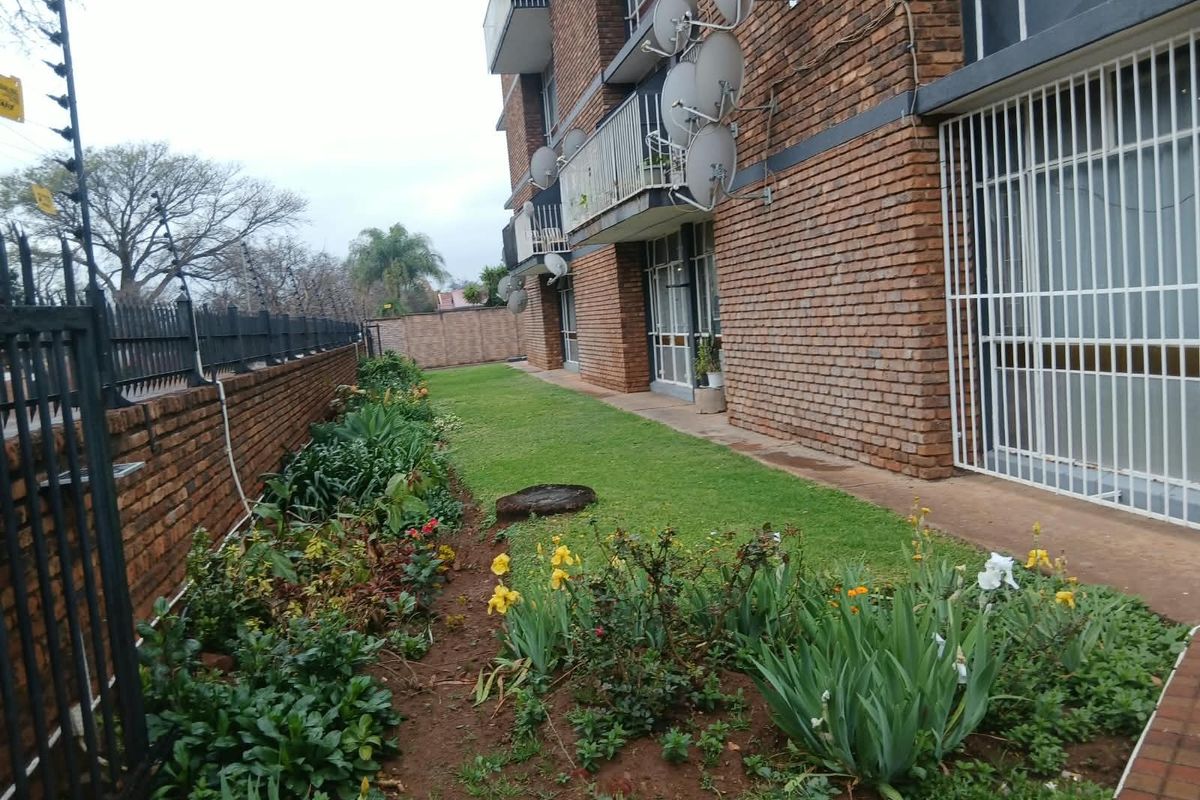 Exterior view of the apartment building featuring a brick facade, ground floor garden area, and security fencing.