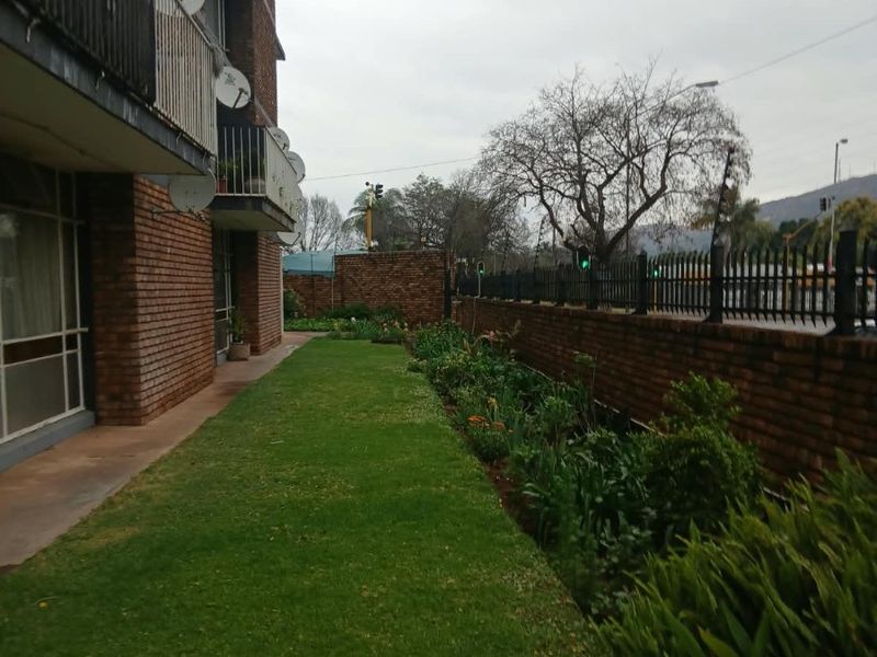 A view of the apartment building's rear exterior, featuring a brick facade, private balconies with metal railings, and a landscaped garden area.