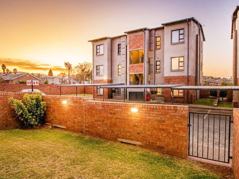 A well-maintained apartment complex featuring face brick exterior walls, secure gated access, paved parking areas, and integrated exterior lighting at sunset.