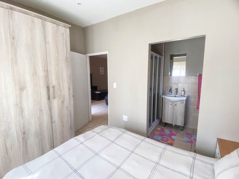 A well-maintained bedroom featuring a built-in wardrobe and an adjoining en-suite bathroom with a shower and vanity basin.