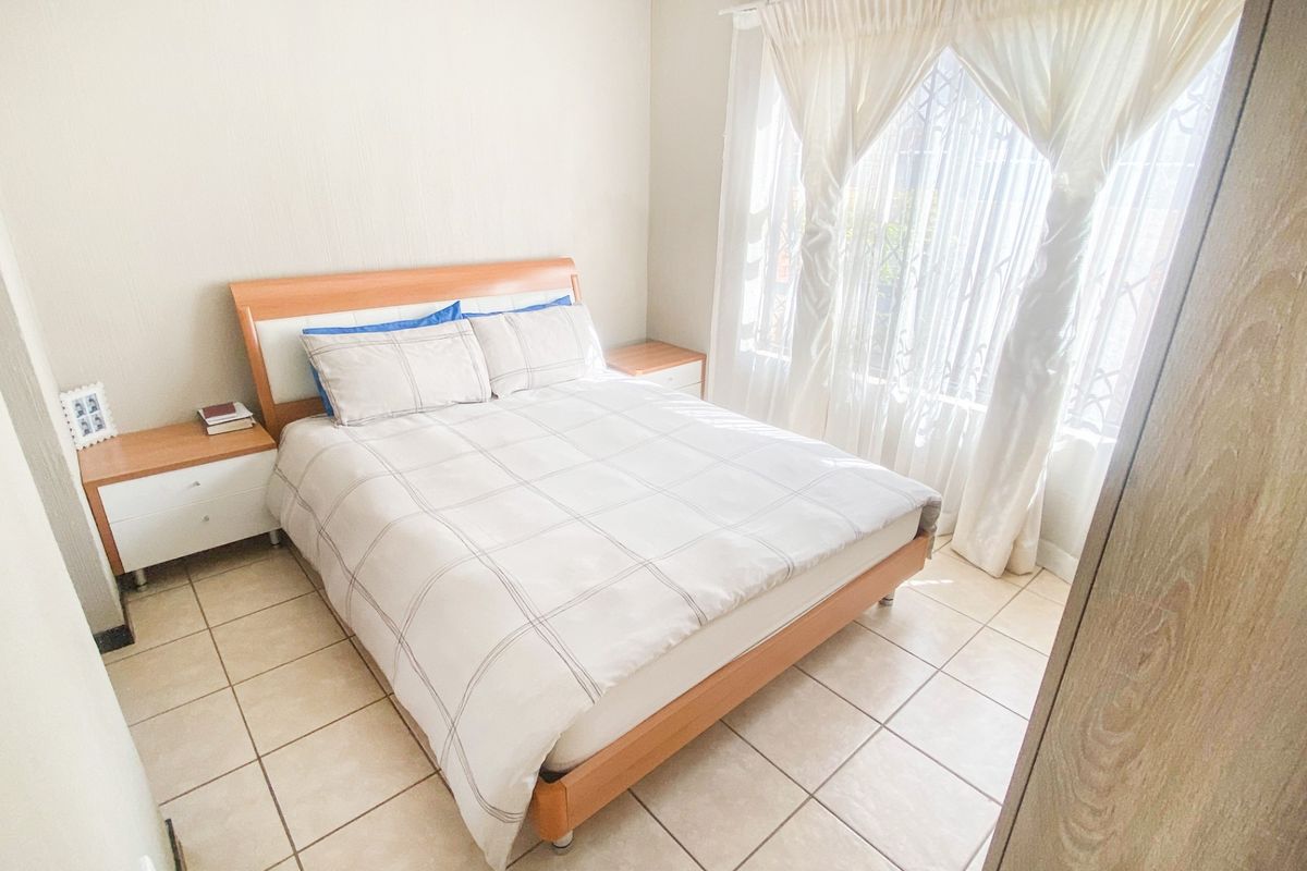 A functional bedroom featuring tiled flooring, a built-in wardrobe, and a window fitted with a security gate.
