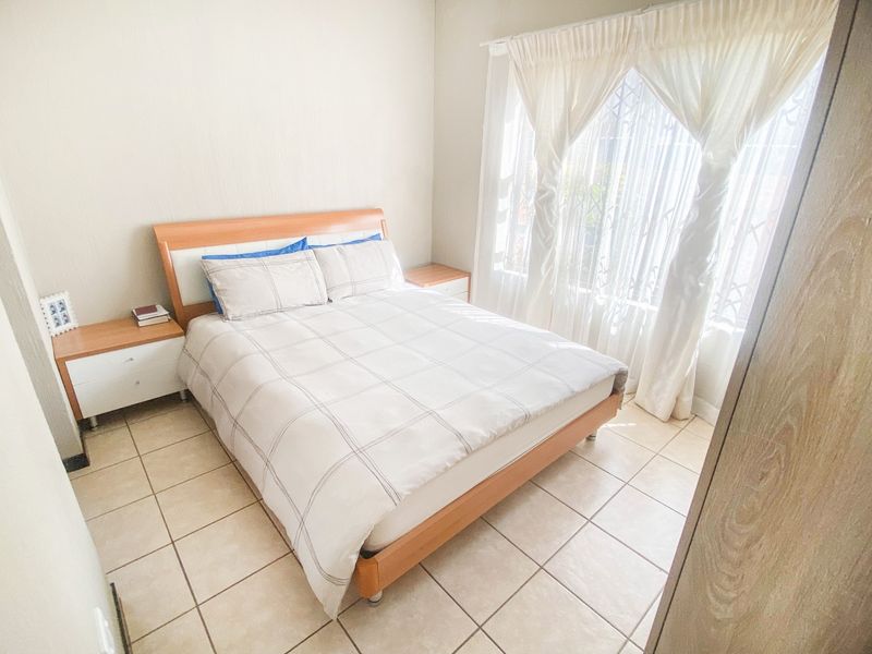 A functional bedroom featuring tiled flooring, a built-in wardrobe, and a window fitted with a security gate.