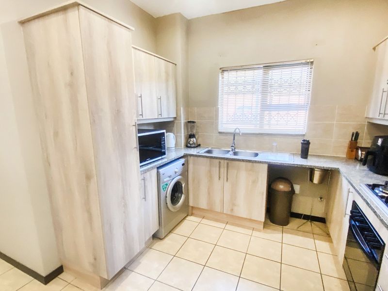 A functional kitchen featuring light wood-finish cabinetry, tiled flooring, a stainless steel sink, and integrated appliance spaces including a built-in oven and hob.