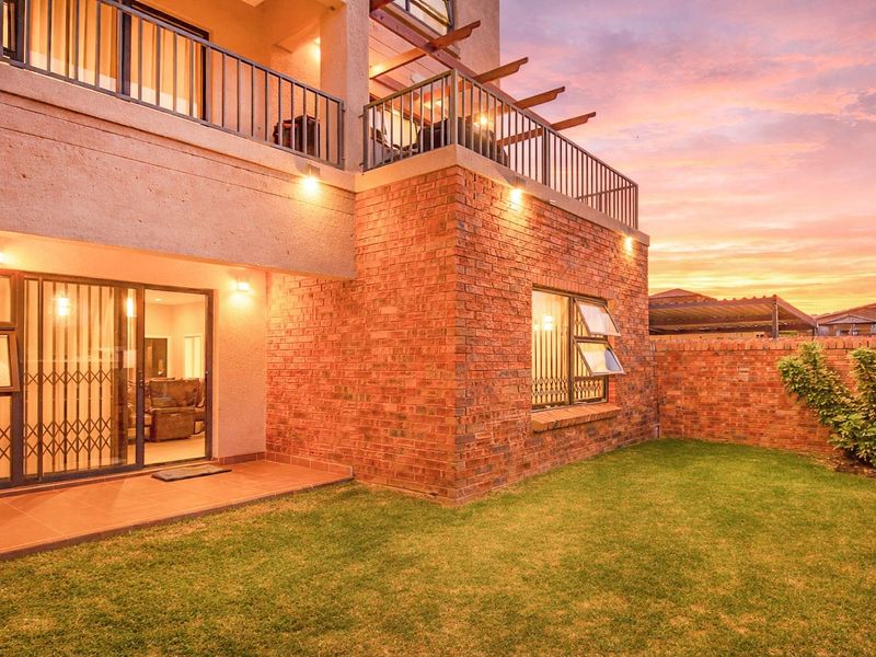 Rear view of the apartment featuring a private garden, brick facade, tiled patio, and an upper-level balcony with metal railings at sunset.