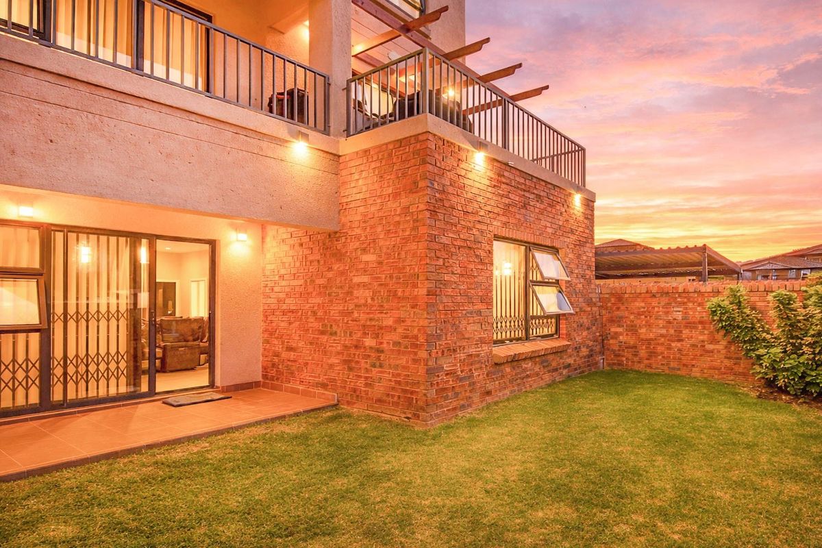 Rear view of the apartment featuring a private garden, brick facade, tiled patio, and an upper-level balcony with metal railings at sunset.