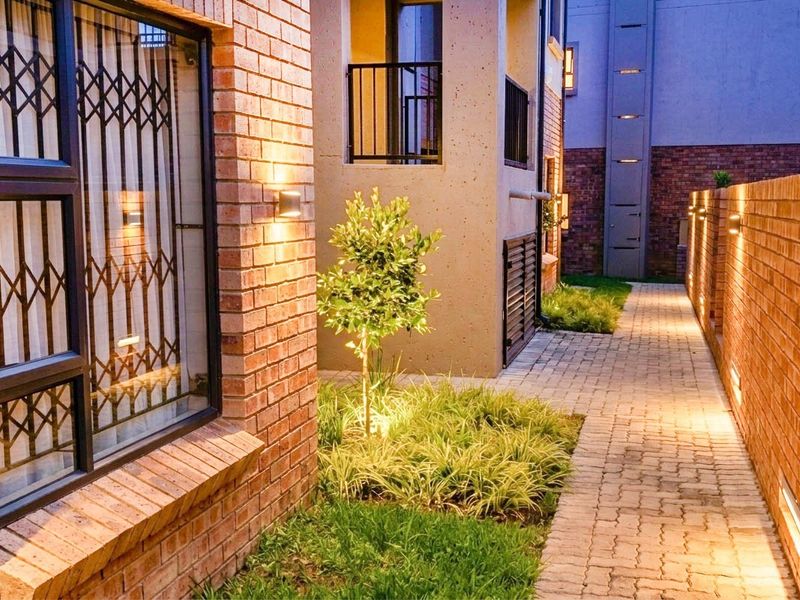 A well-maintained rear exterior area featuring a brick facade, paved walkway, and integrated wall lighting, creating a warm and secure atmosphere.