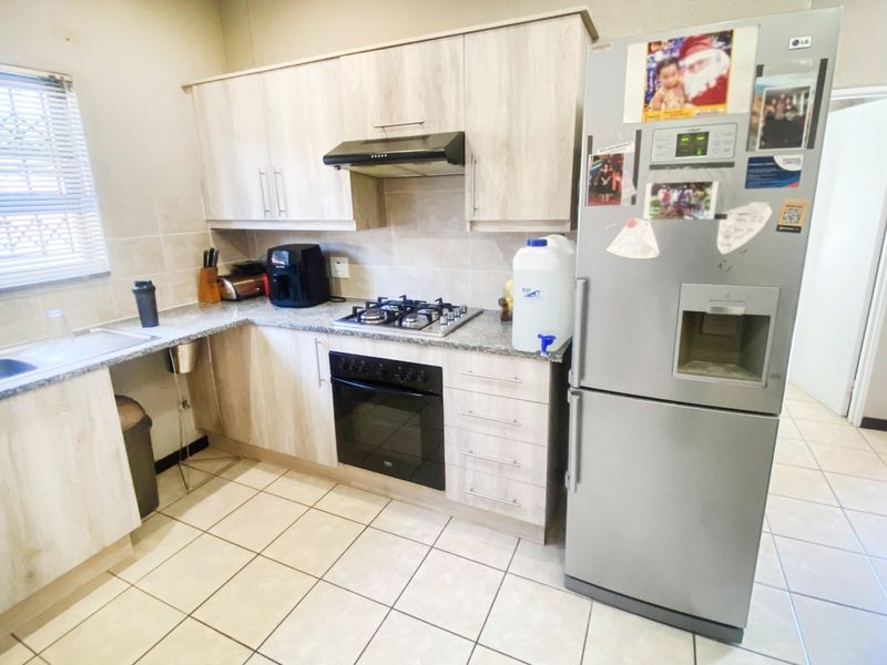 A functional kitchen featuring light wood-grain cabinetry, granite countertops, a gas hob with extractor fan, and tiled flooring throughout.