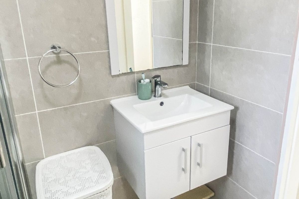 A modern bathroom featuring a wall-mounted vanity with a ceramic basin, mixer tap, wall mirror, and neutral tiled finishes throughout.