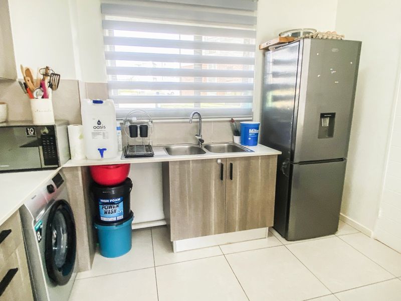 A functional laundry area featuring a double bowl stainless steel sink, laminate cabinetry, and tiled flooring, providing practical utility space.