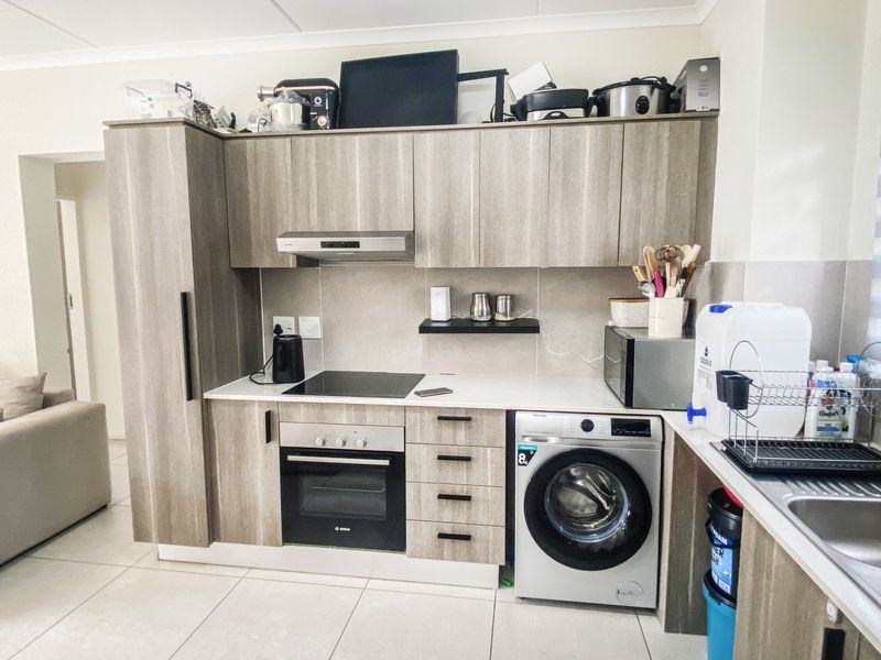 Modern kitchen featuring wood-grain cabinetry, integrated washing machine, electric hob, oven, and a tiled backsplash with neutral floor tiles.