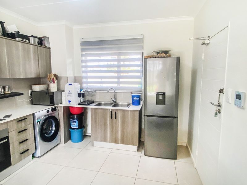 A functional kitchen featuring modern wood-finish cabinetry, tiled flooring, a double sink, and a window with a roller blind.