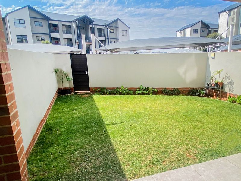 A private rear garden featuring a well-maintained lawn, boundary walls, a pedestrian gate, and a paved patio area with shade sail coverage.