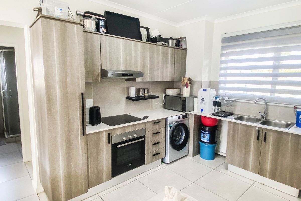 Modern kitchen featuring wood-look cabinetry, integrated electric hob and oven, extractor fan, double sink, and tiled flooring with ample natural light.