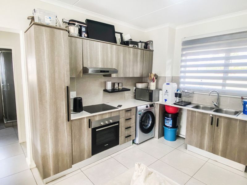 Modern kitchen featuring wood-look cabinetry, integrated electric hob and oven, extractor fan, double sink, and tiled flooring with ample natural light.