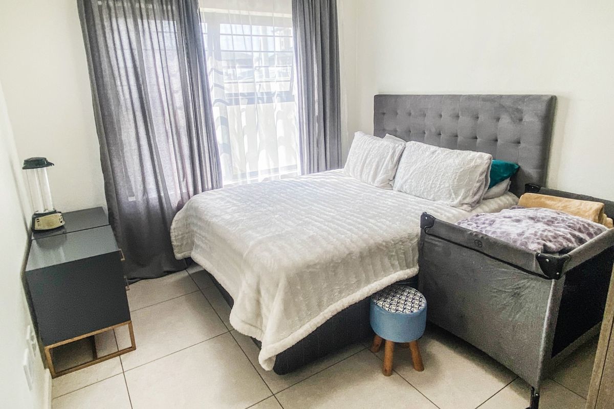 A well-maintained bedroom featuring neutral tiled flooring and large windows with installed curtain rails, providing a bright and functional living space.