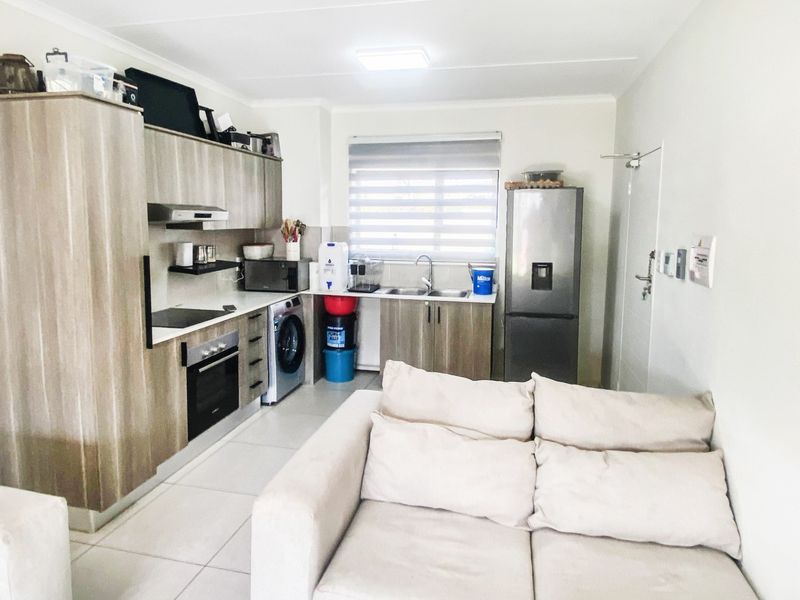 Open-plan kitchen featuring modern wood-look cabinetry, integrated appliances, and tiled flooring, seamlessly connected to the living area.