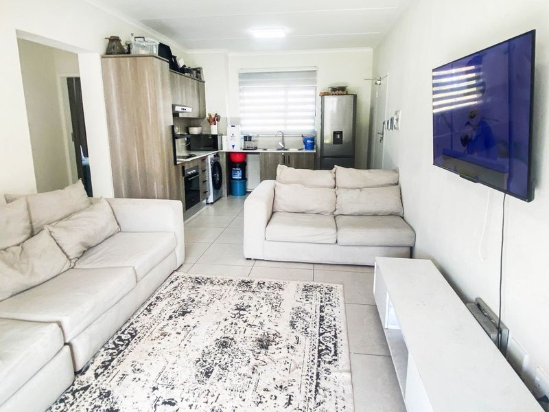 Open-plan living area featuring a compact kitchen with built-in cabinetry, integrated appliances, and tiled flooring throughout, creating a functional and connected living space.
