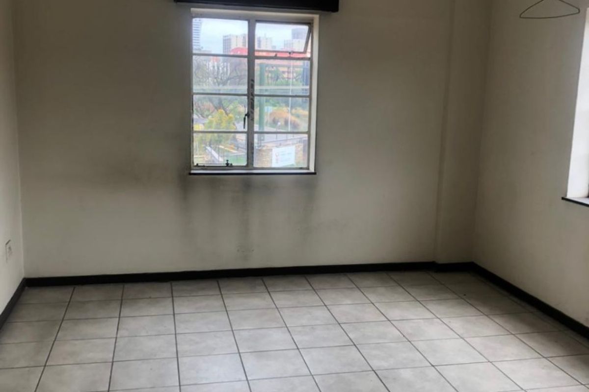 An empty bedroom featuring tiled flooring with visible cracks and wall staining below the window, offering a blank canvas for renovation.