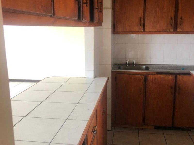 A dated kitchen featuring wooden cabinetry, tiled countertops, and a stainless steel sink, offering a functional layout ready for modernization.