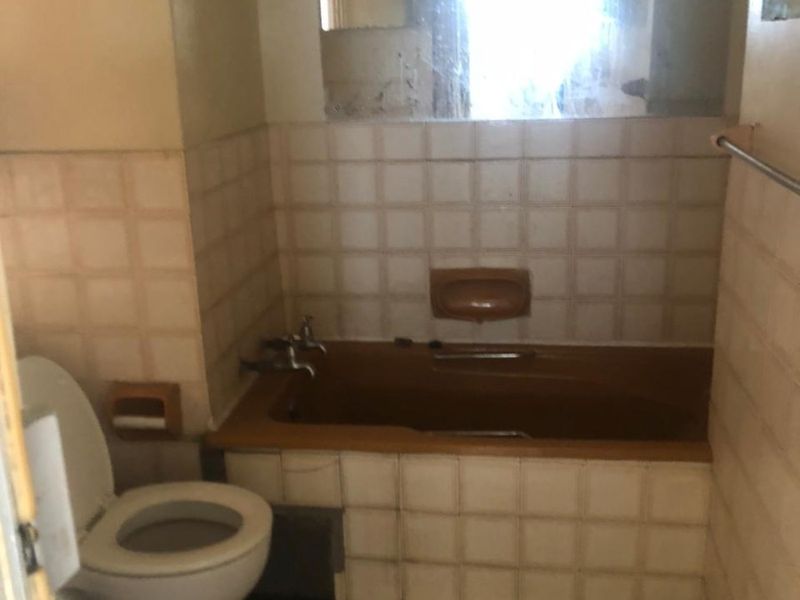 A dated bathroom featuring a built-in bathtub, ceramic tiling, and a toilet, requiring modernization and cosmetic updates to improve its overall condition.