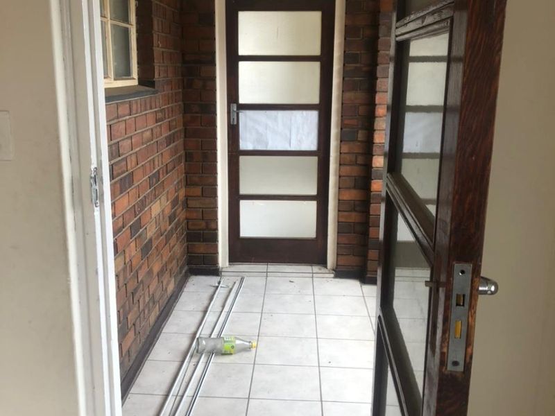A covered outdoor patio area featuring exposed brick walls, tiled flooring, and a timber-framed glass door leading to the interior.