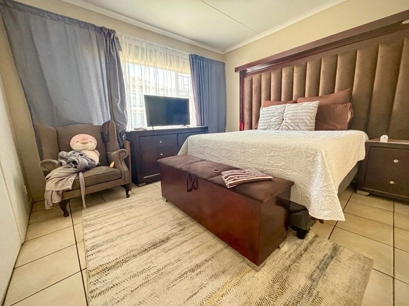 A spacious bedroom featuring tiled flooring and a large, integrated upholstered headboard, offering a comfortable and functional sleeping area.