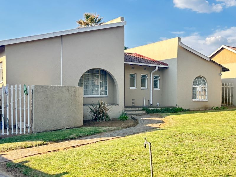 Front view of a single-story house featuring arched windows, a paved walkway, and a well-maintained lawn area.