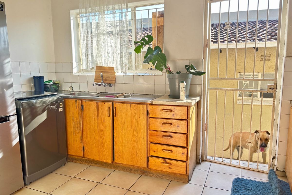 A functional kitchen area featuring wooden cabinetry, a stainless steel sink, tiled splashback, and direct access to the exterior via a security gate.
