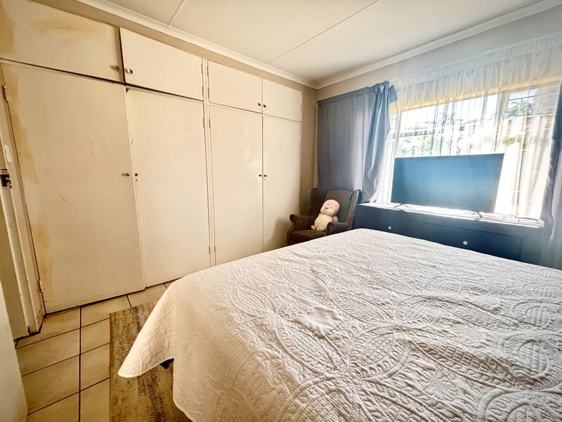 Bedroom featuring built-in cupboards, tiled flooring, and security bars on the window. The room shows signs of wear and ceiling water damage.
