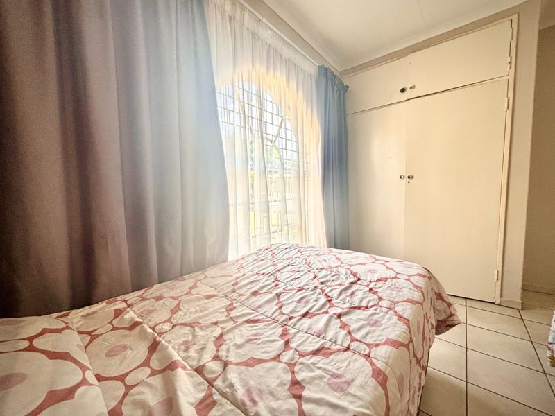 A bedroom featuring built-in cupboards, tiled flooring, and an arched window with security bars, offering a functional and well-lit living space.