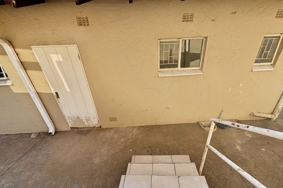 Rear exterior view showing a concrete patio area with tiled steps, metal handrail, and access door with visible wear.