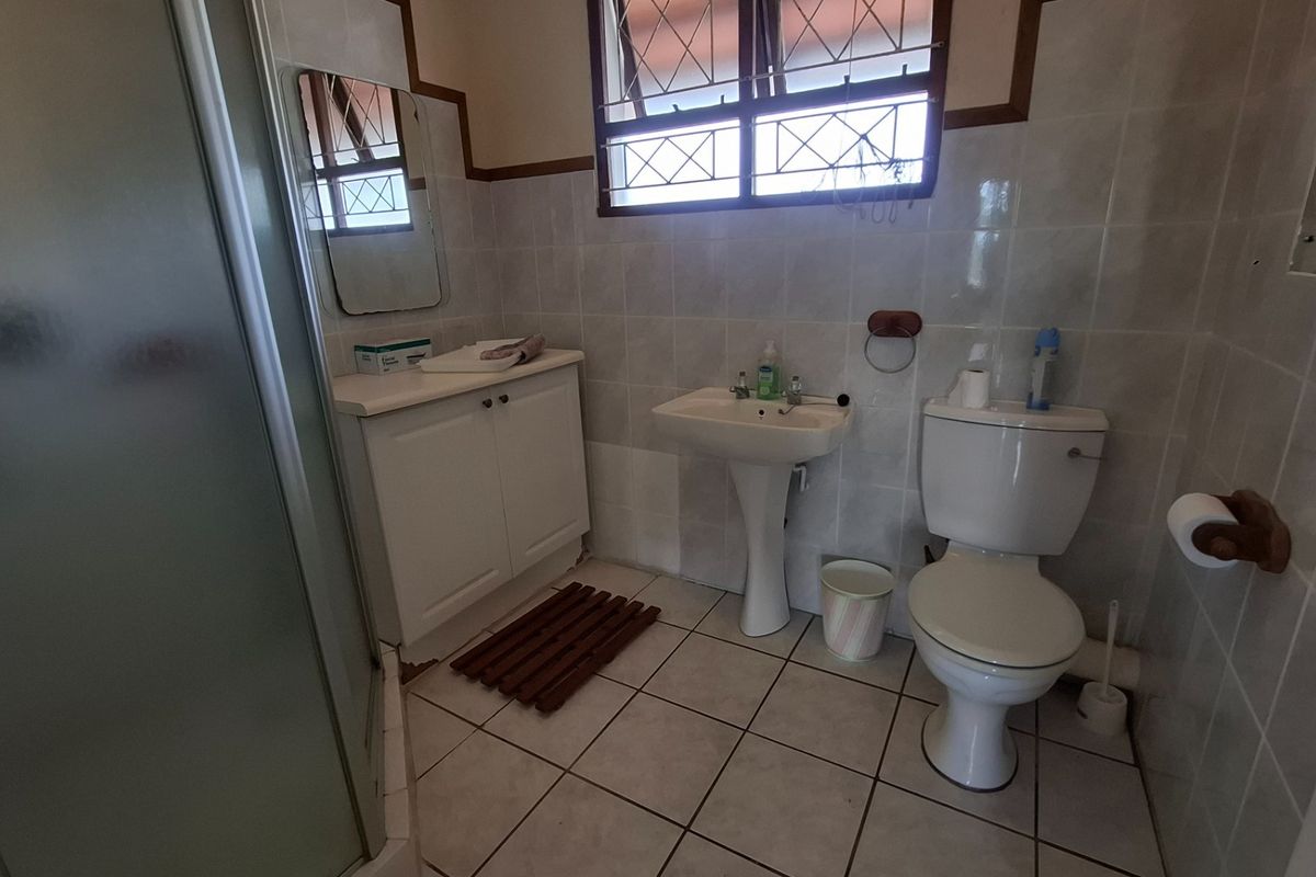 A functional bathroom featuring a pedestal basin, toilet, shower enclosure, and vanity cabinet with tiled walls and flooring.