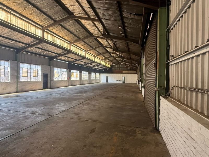 Spacious industrial warehouse featuring high ceilings with exposed steel trusses, concrete flooring, and large clerestory windows providing ample natural light.