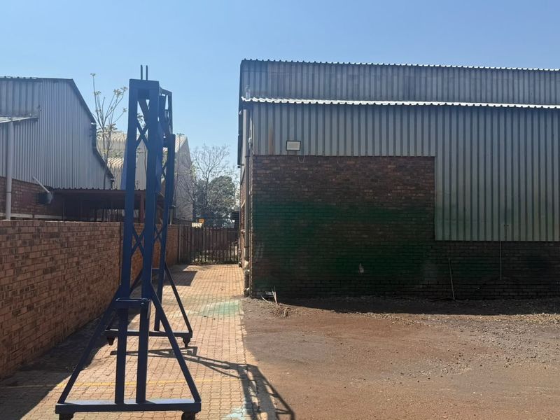 Rear exterior view of an industrial property featuring corrugated metal cladding, brick boundary walls, and a paved access area.