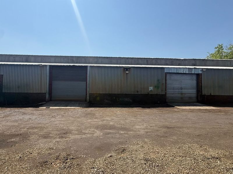 Industrial warehouse exterior featuring corrugated metal cladding, two large roller shutter doors, and a spacious unpaved yard area.
