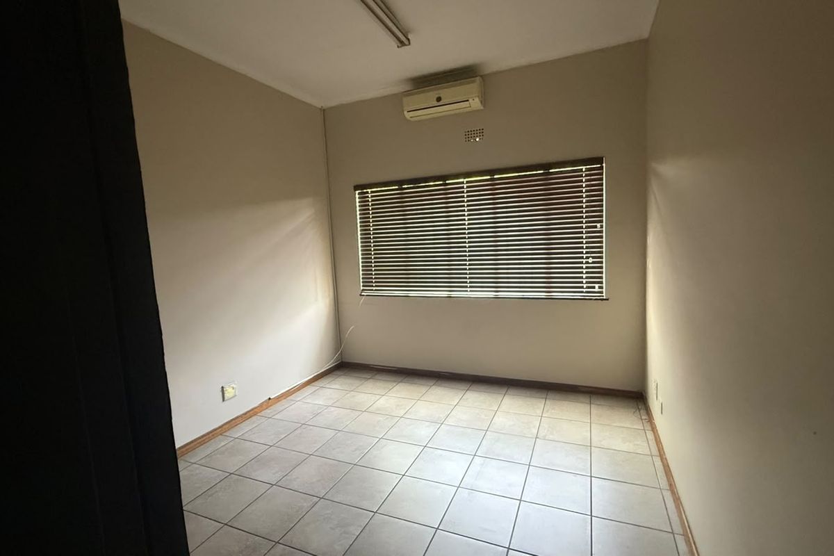 A vacant bedroom featuring tiled flooring, a wall-mounted air conditioning unit, and window blinds, offering a neutral space ready for customization.