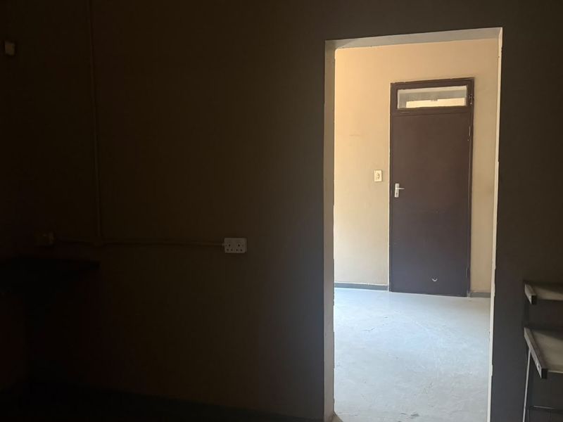 An empty utility or storage space featuring security bars on the window and an internal door leading to an adjacent room.