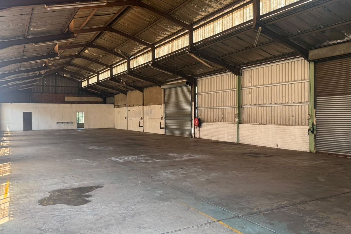 Spacious industrial warehouse featuring high ceilings with exposed steel trusses, concrete flooring, and multiple roller shutter doors for efficient access.