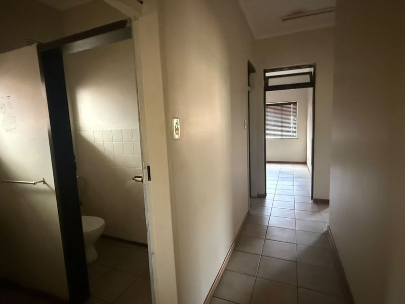 A functional hallway connecting multiple rooms, featuring tiled flooring and neutral wall finishes, providing access to a bathroom and adjacent living spaces.
