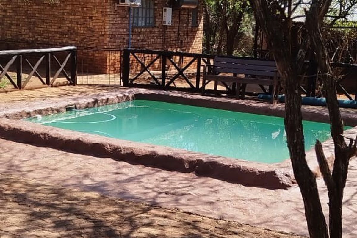 Outdoor pool area featuring a paved surround, brick building facade, and timber fencing, set within a natural garden environment.