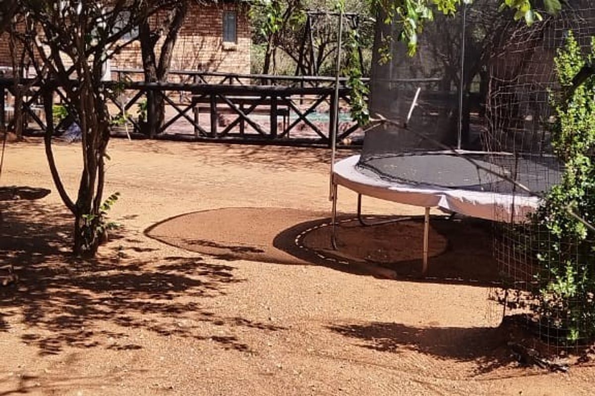 A spacious, natural garden area featuring mature trees and wooden perimeter fencing, providing a rustic outdoor setting.